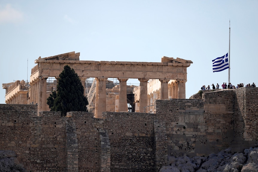 The Greek flag flies at half-mast in front of the Parthenon temple