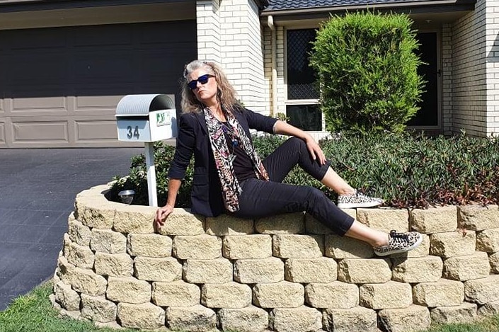 A woman sits on her garden and strikes a pose