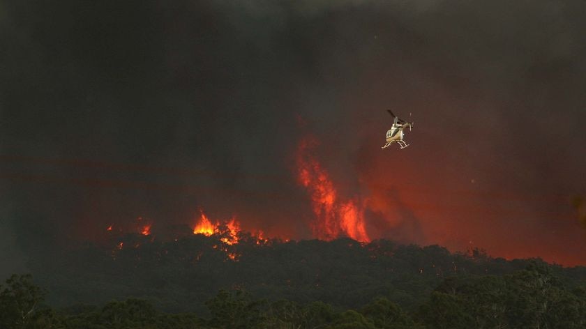 A fire-fighting helicopter approaches an out of control bushfire in the Bunyip State Park