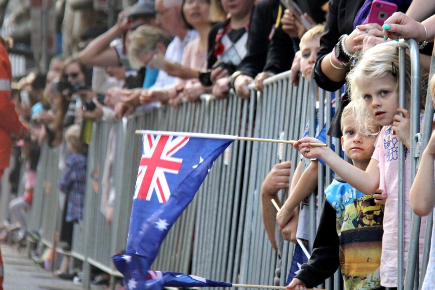 View looking down the barriers of two children leaning out from a barrier and waving small Australian flags.
