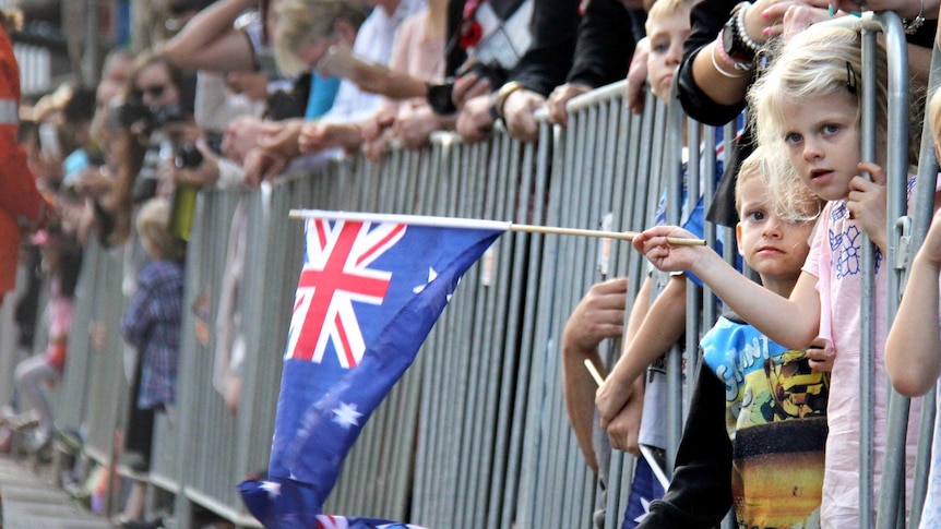 View looking down the barriers of two children leaning out from a barrier and waving small Australian flags.