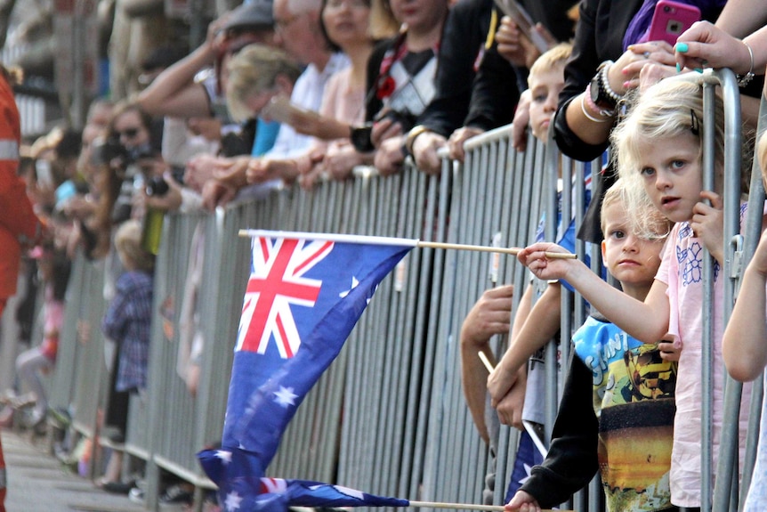 View looking down the barriers of two children leaning out from a barrier and waving small Australian flags.