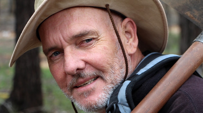 A man with a broadbrim hat mining for gold with a metal detector