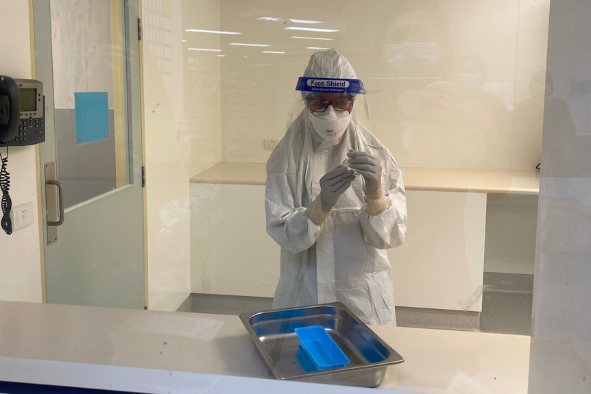 A pharmacist in full PPE prepares a vial of a drug.