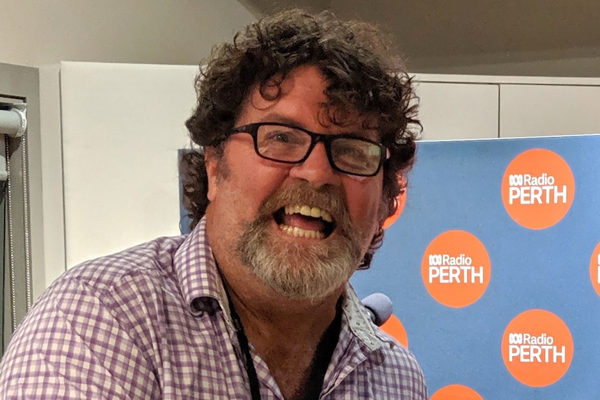 A tigh head and shoulders shot of a smiling Russell Woolf wearing a checked shirt in a radio studio.