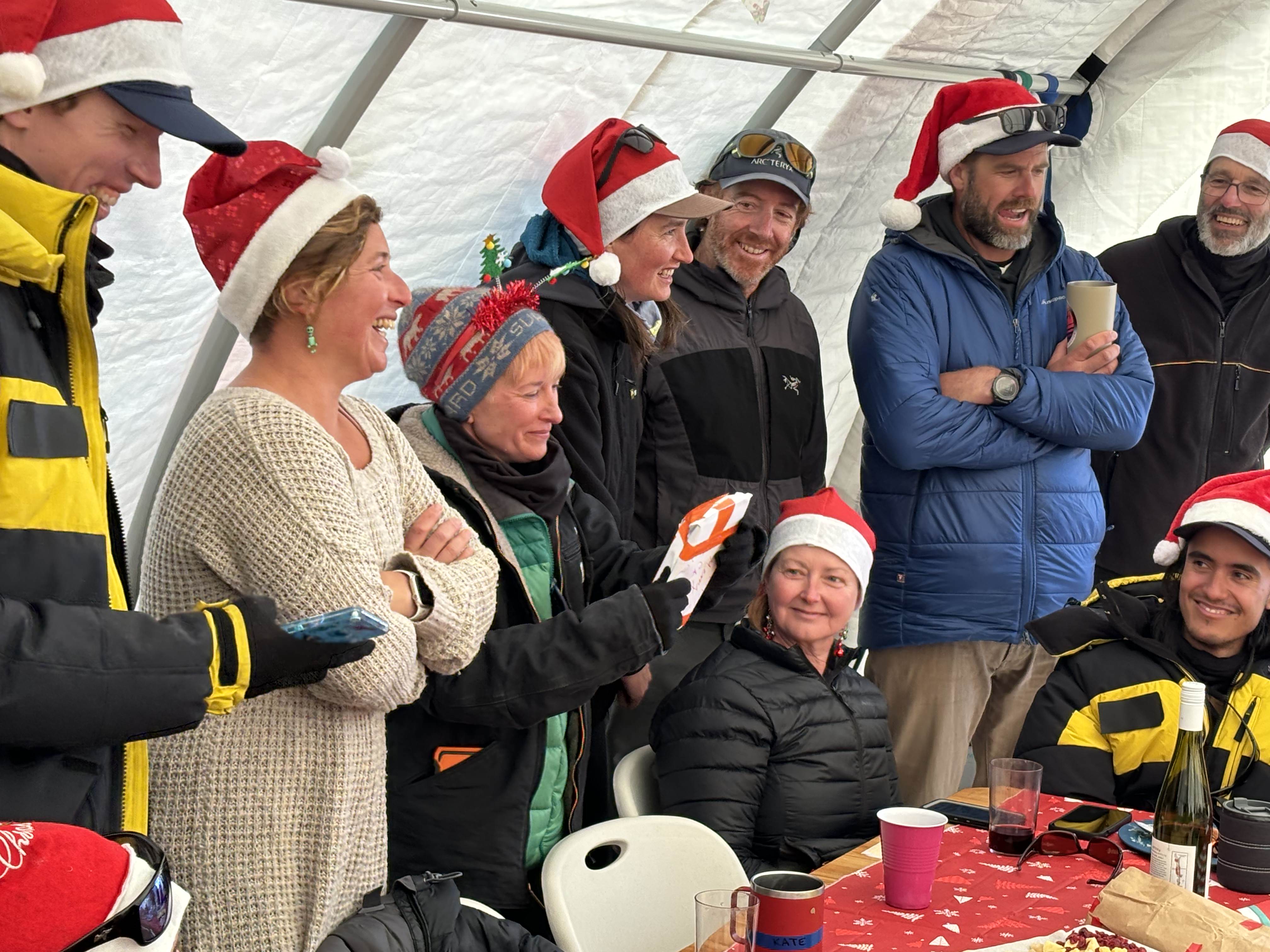 A bunch of people laughing and wearing Christmas hats