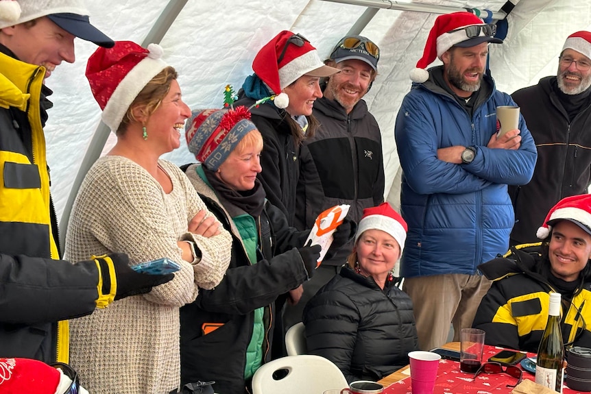A bunch of people laughing and wearing Christmas hats