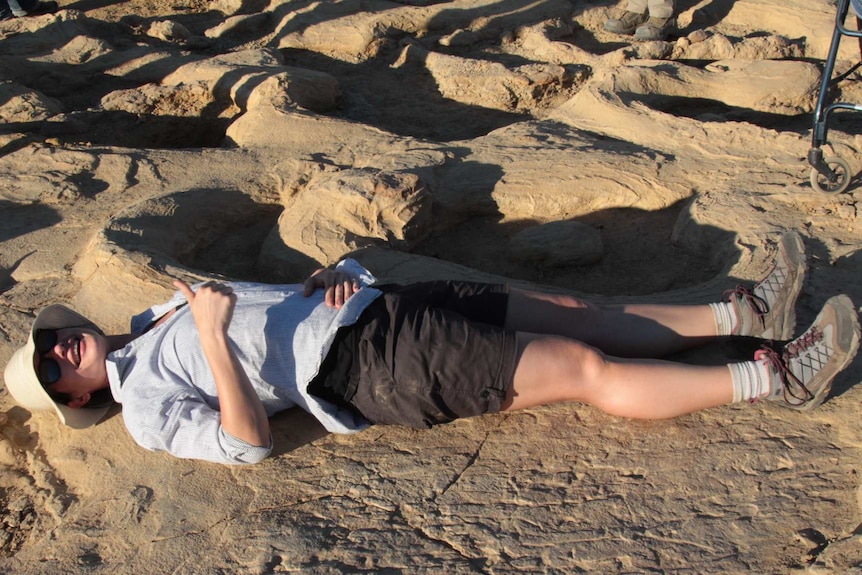 A woman lies beside dinosaur footprints.