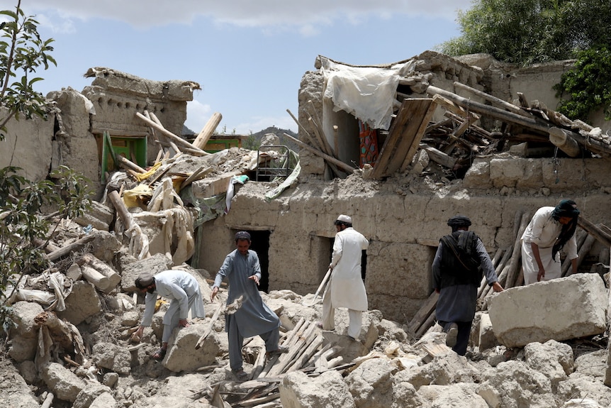 Five men search through the rubble of a collapsed building.