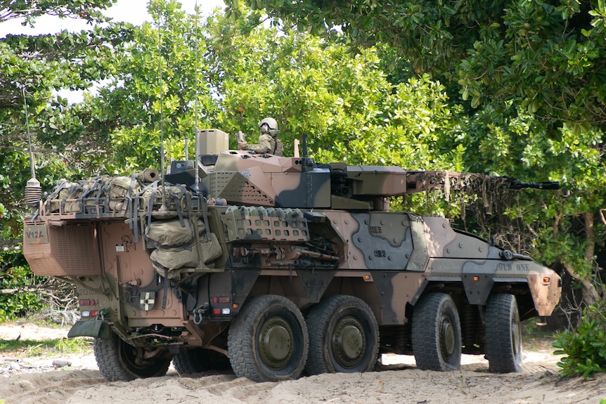 Camouflage-painted Army vehicle with gun turret drives among trees 