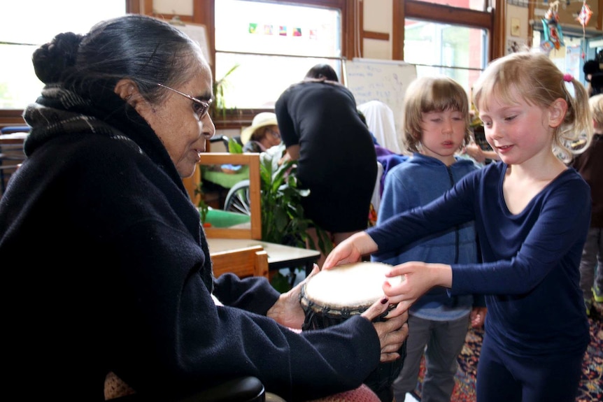 Child hands drum to aged care resident