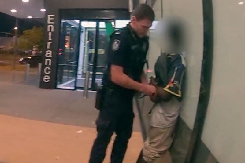 A young person is pushed against a wall while police put handcuffs on them