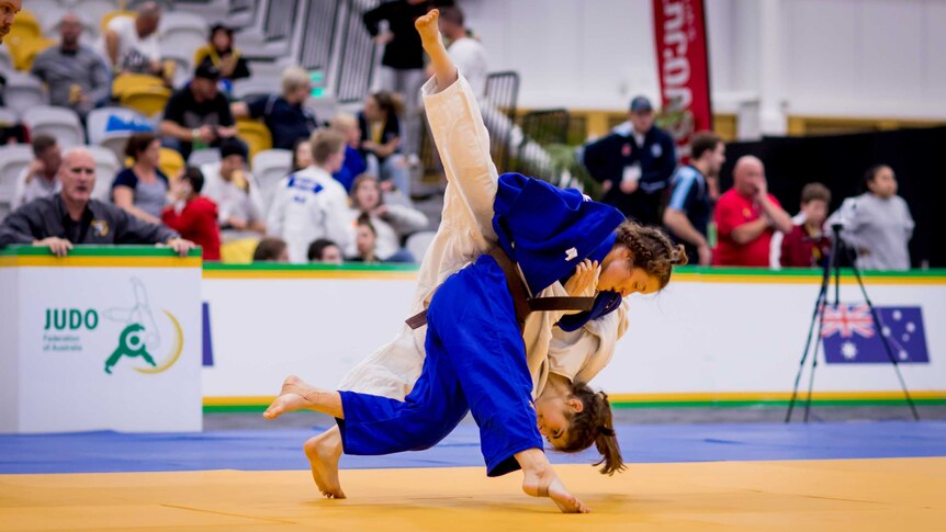 Sophie Robins (in blue) throws a competitor, whose legs fly up into the air.