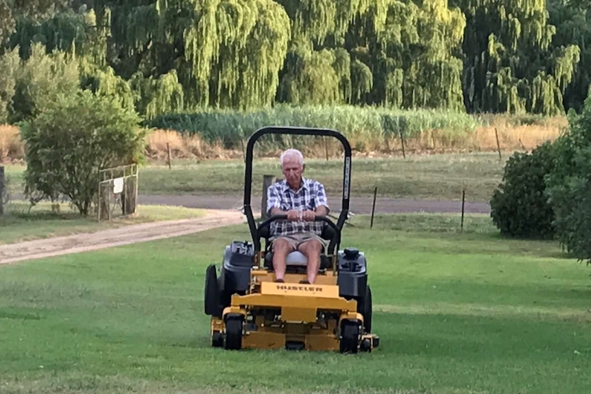 An elderly man with white hair on a ride-on mower
