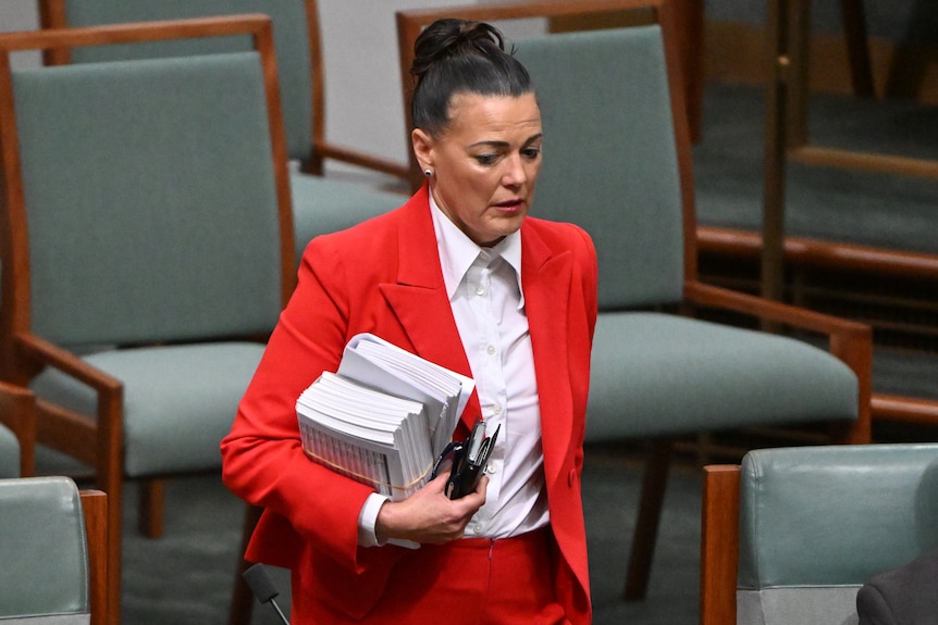 Libby in parliament with documents in a red suit