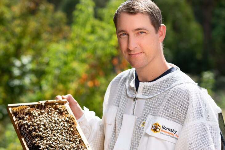 Dr John Roberts holding a bee-hive in front of green trees.