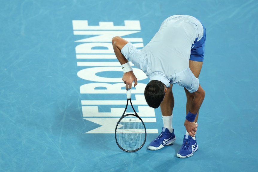 A man bends over in pain while standing on a blue tennis court.