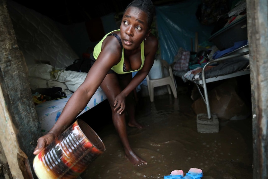 A woman uses a big tin to get water out of her house.