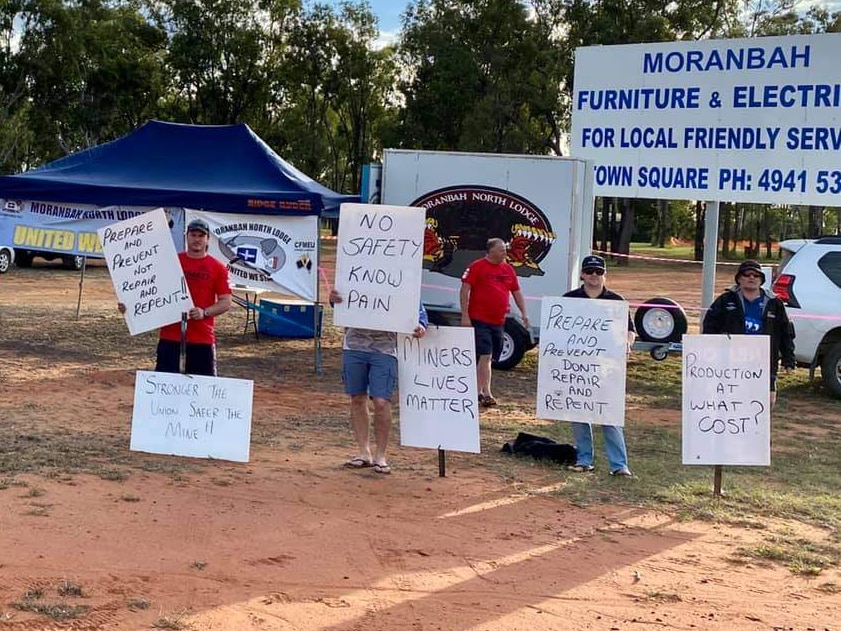 Coal mine workers holding signs by the side of a road.