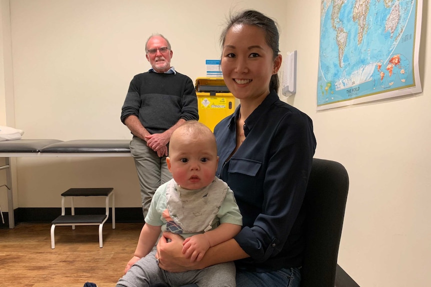 A woman holding a baby with an older man behind