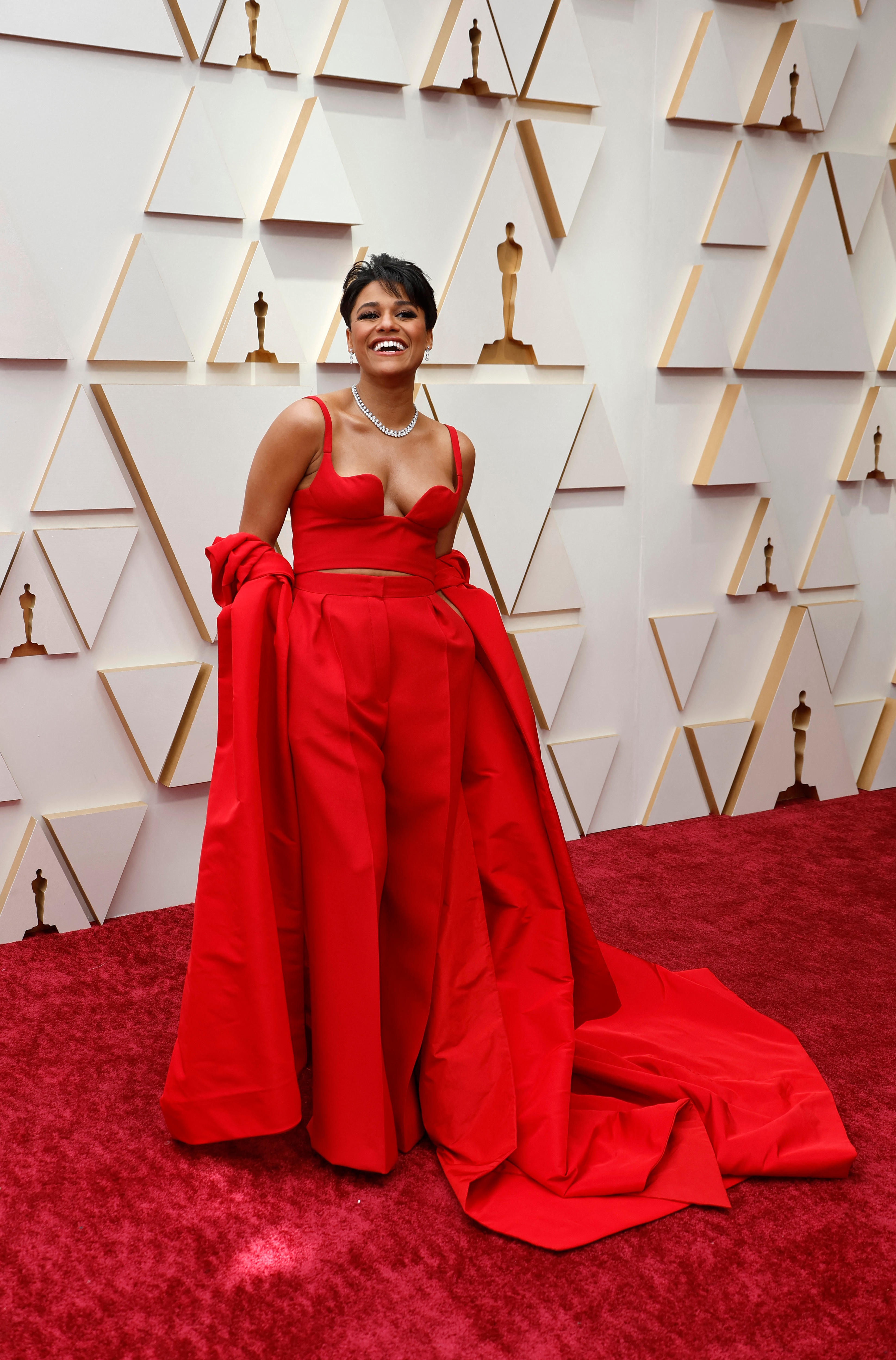 Une femme vêtue d'une robe rouge se tient debout sur un tapis rouge devant un mur médiatique blanc aux Oscars.