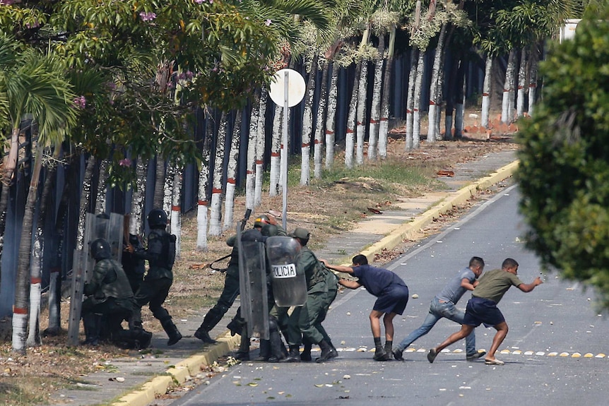 Police crouch behind plastic shields as some in civilians clothing run away.