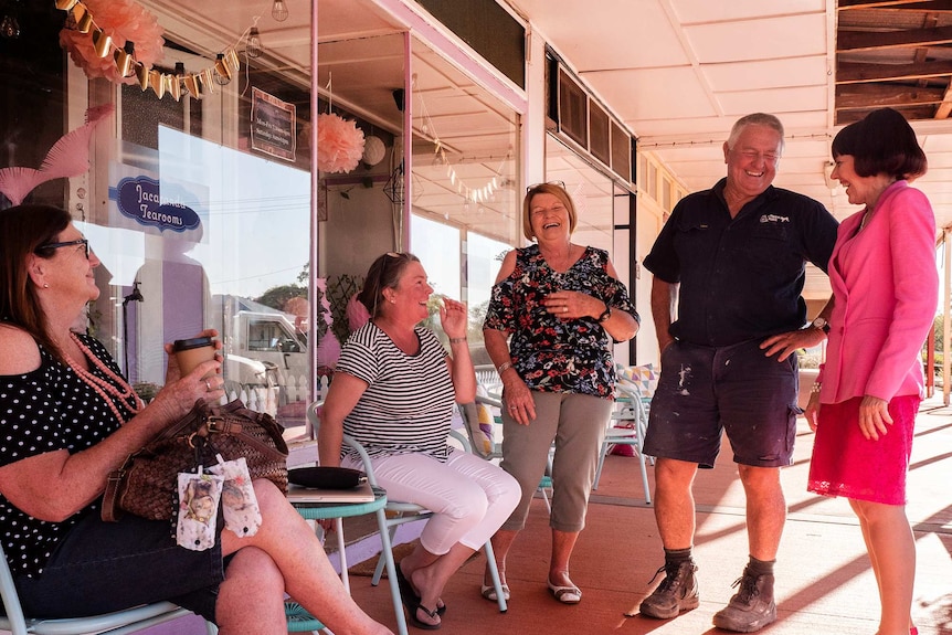 A group of people laughing outside a country style shop.