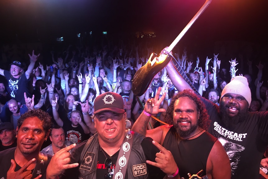 Four male band members posing at their metal band concert while the crowd is behind them. 