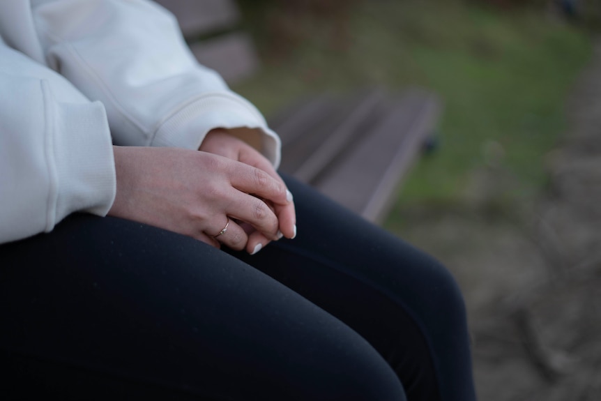 Woman's hands resting in her lap. She is seated on a park bench.