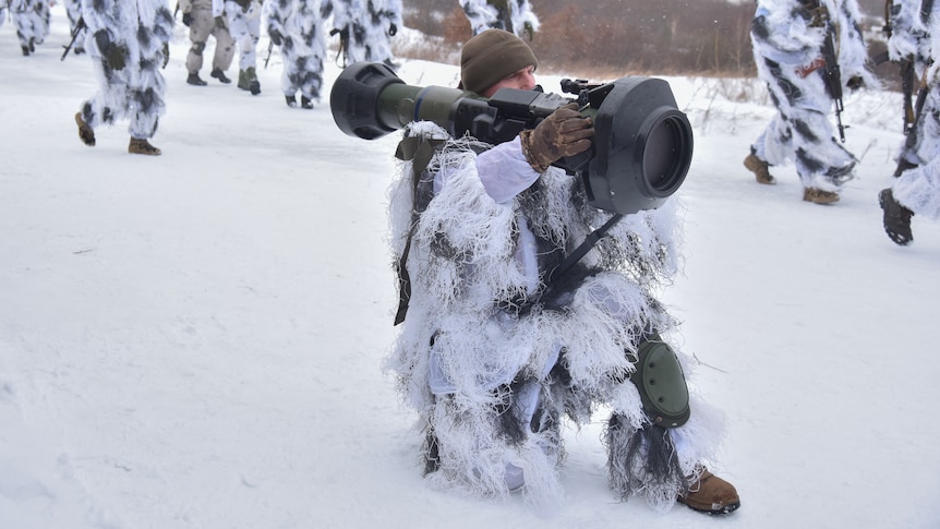 A soldier kneeling in the snow with an anti-tank missile launcher on his shoulder.