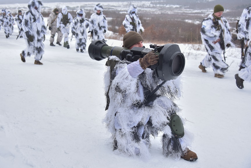 A soldier kneeling in the snow with an anti-tank missile launcher on his shoulder.