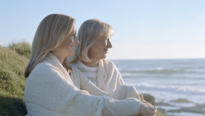 Mother and mature daughter sitting on ground by ocean, smiling (Thinkstock: Valueline)