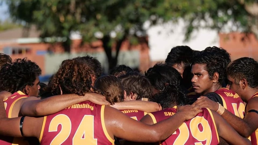 Football players stand in a huddle.