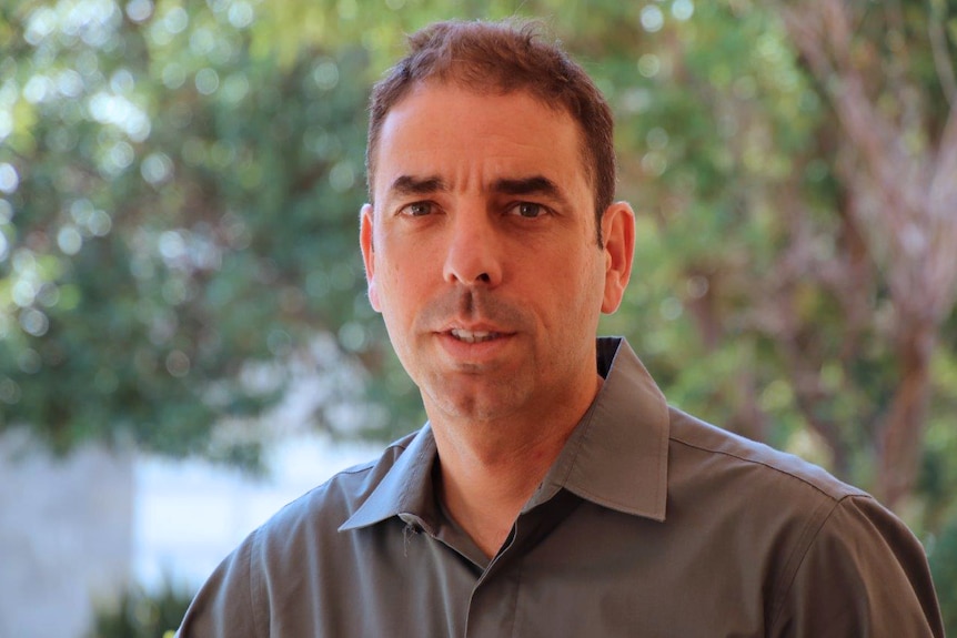 A head and shoulders shot of a middle aged man with short dark hair posing for a photo outdoors.