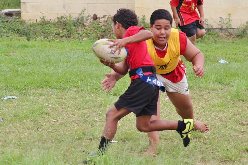 A boy carrying a rugby ball is grabbed by his opponent.