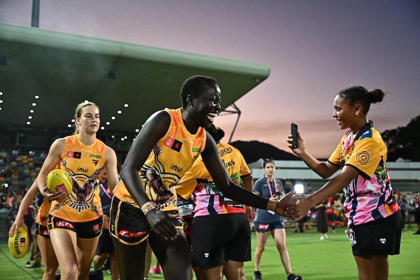 Akec Makur Chot hi-fives a young woman as she walks onto the field in Cairns playing AFLW for Hawthorn