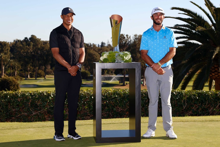 Golfers Tiger Woods and Max Homa stand either side of a silver trophy. There are palm trees in the background.