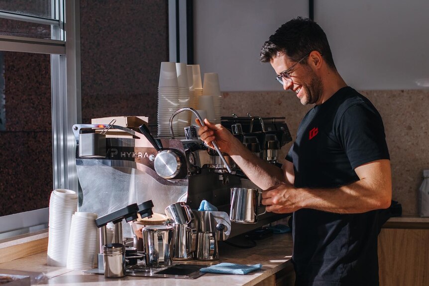 A man with dark hair and a black shirt makes a coffee on a machine
