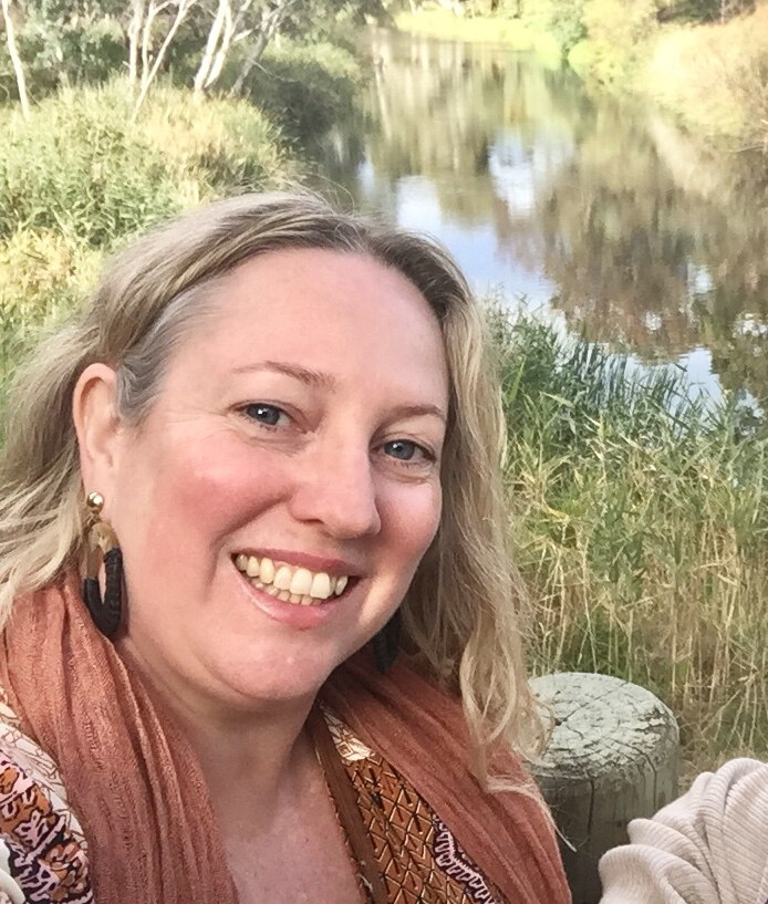 Vanessa Phillips stands, smiling, in front of a local creek.