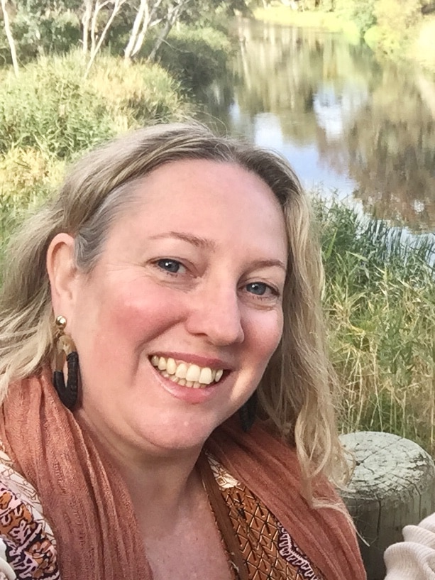 Vanessa Phillips stands, smiling, in front of a local creek.