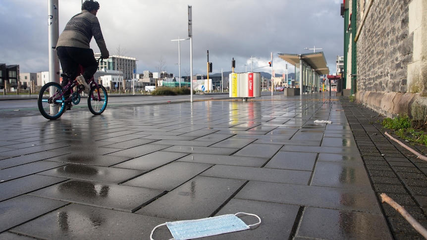 A cyclist rides past a discarded face mask on an empty street in Christchurch