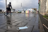 A cyclist rides past a discarded face mask on an empty street in Christchurch