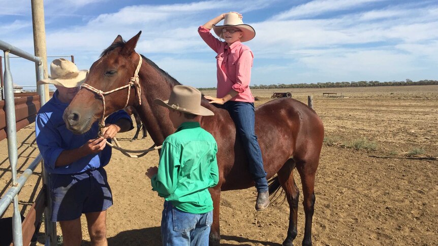 11-year-old Ruby Dyer sitting on horse as Dad and brother 12-year-old Sam help with fix the reigns.