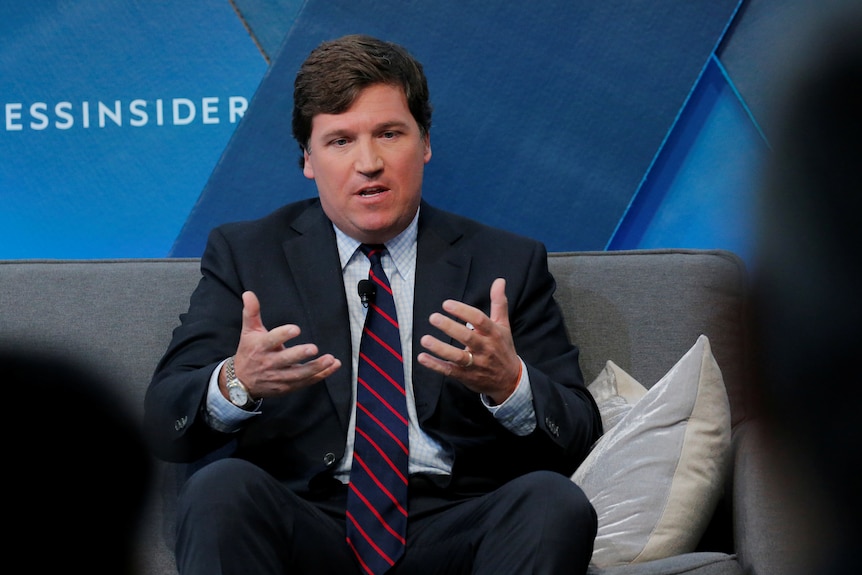 Fox News host Tucker Carlson gesticulating while talking on a couch