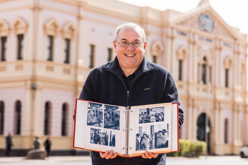 man stands in front of town hall with photo album