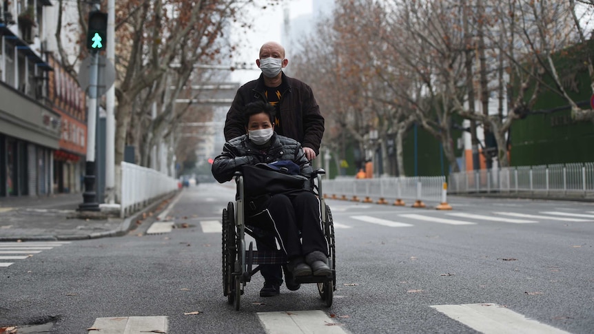 A man wearing a face mask pushes a woman on a wheelchair in Wuhan.