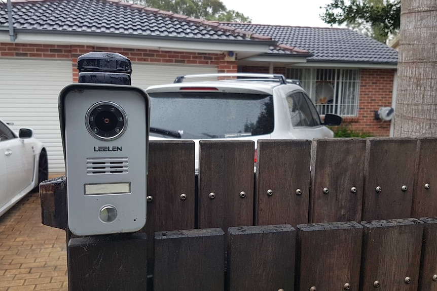 Closeup of intercom outside a suburban home with two cars out the front.