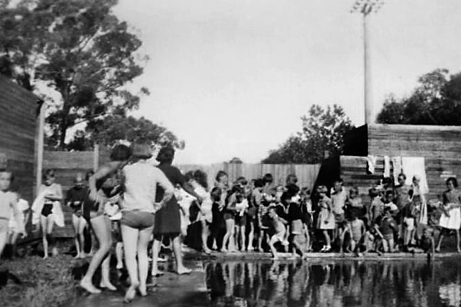 A black-and-white photo of a swimming pool surrounded by children.