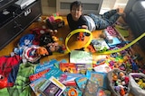 A young boy lying on the floor with a lots of toys and books.