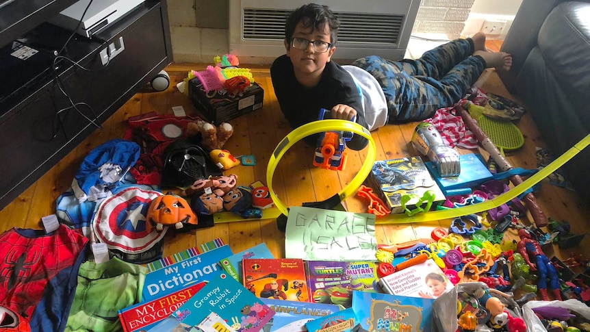 A young boy lying on the floor with a lots of toys and books.